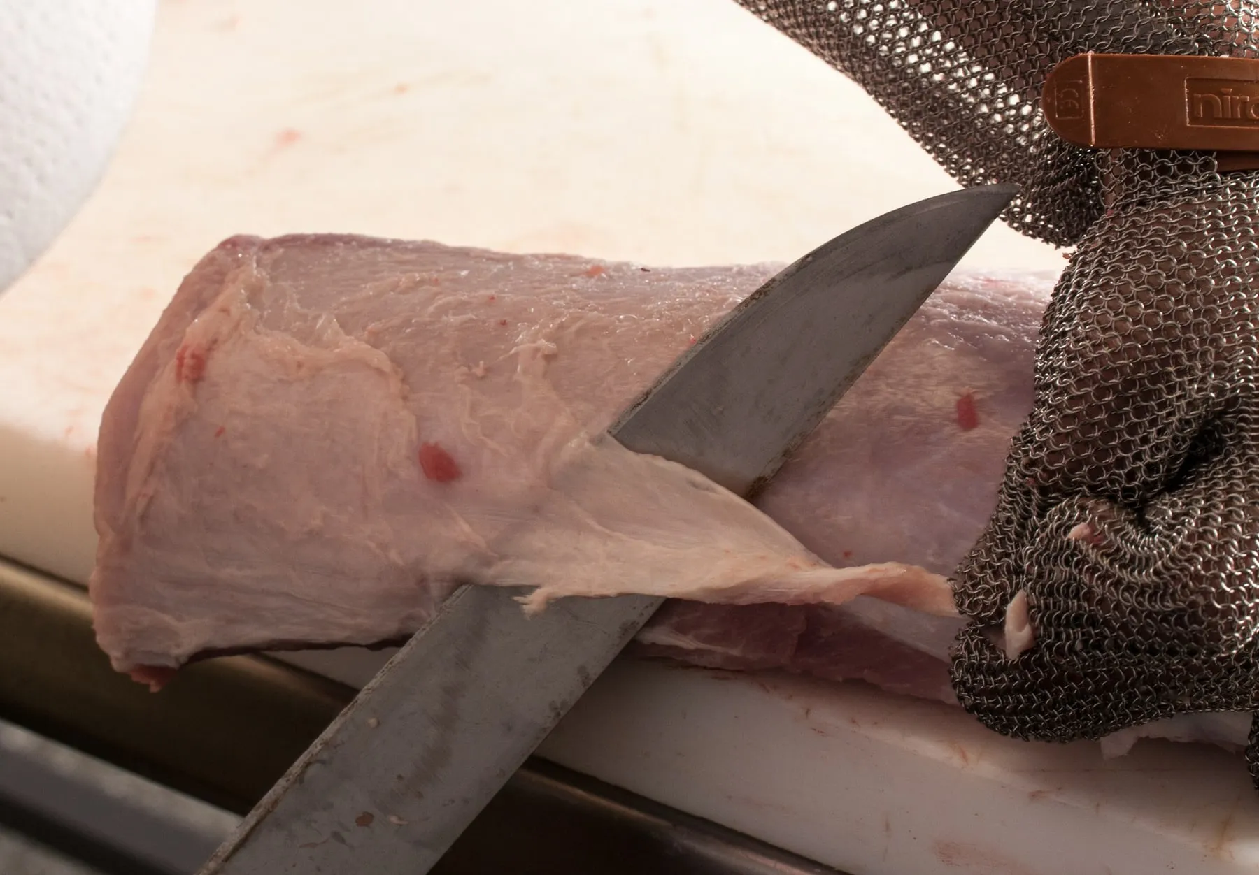 Carnicero cortando una pieza con cuchilla y guante de malla